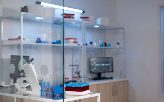 Female scientist looking into a microscope with computer in the background.