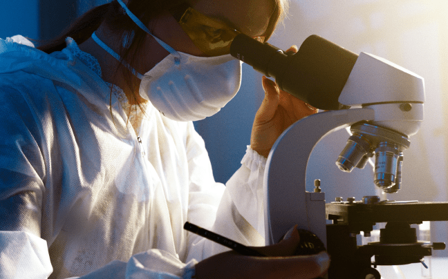 scientist wearing mask and looking into microscope