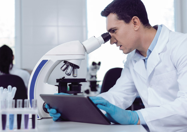 male scientist looking into microscope while using BTLIMS on tablet