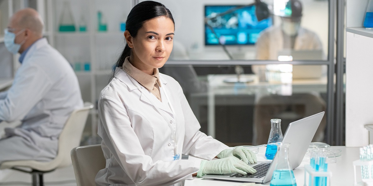 researcher in lab coat and gloves typing in front of laptop