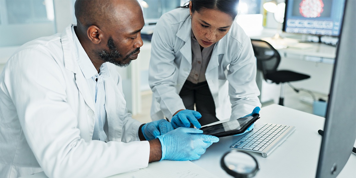 scientists wearing lab coats and blue gloves using a tablet