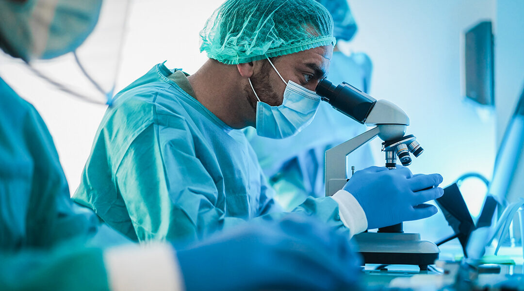 Medical workers in hazmat suit working with microscope and laptop in microbiology lab