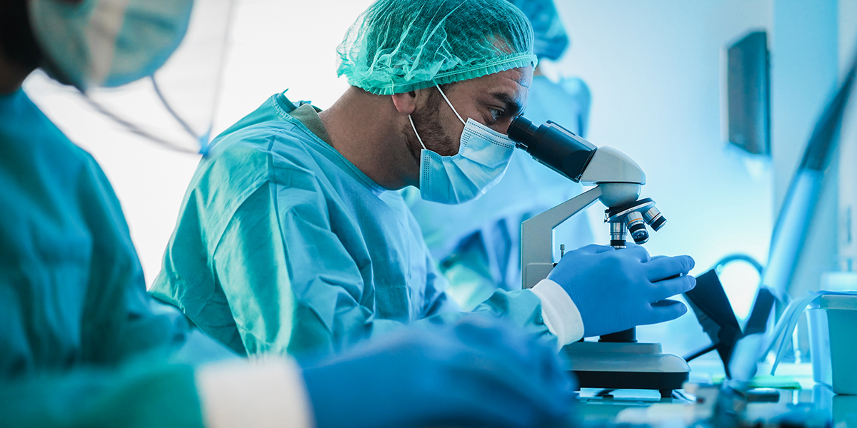 Medical workers in hazmat suit working with microscope and laptop in microbiology lab