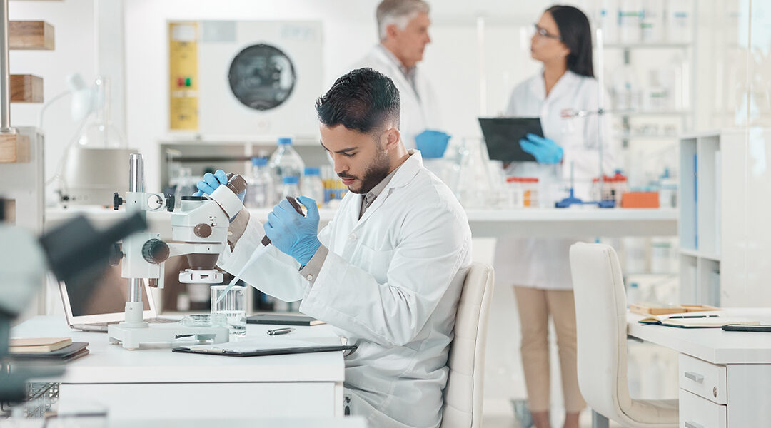 scientist using microscope in laboratory with colleges in background