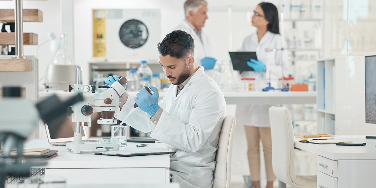 scientist using microscope in laboratory with colleges in background